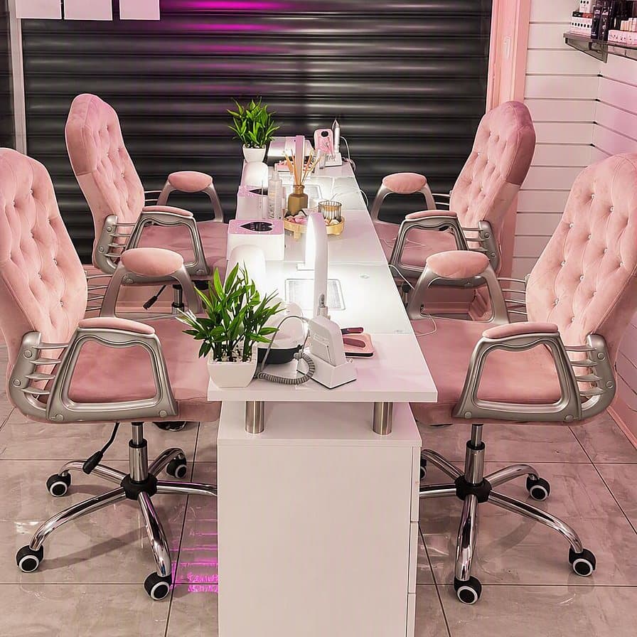 Our beauty nail bar — pink tufted chairs at the white manicure table beneath the magenta salon lighting